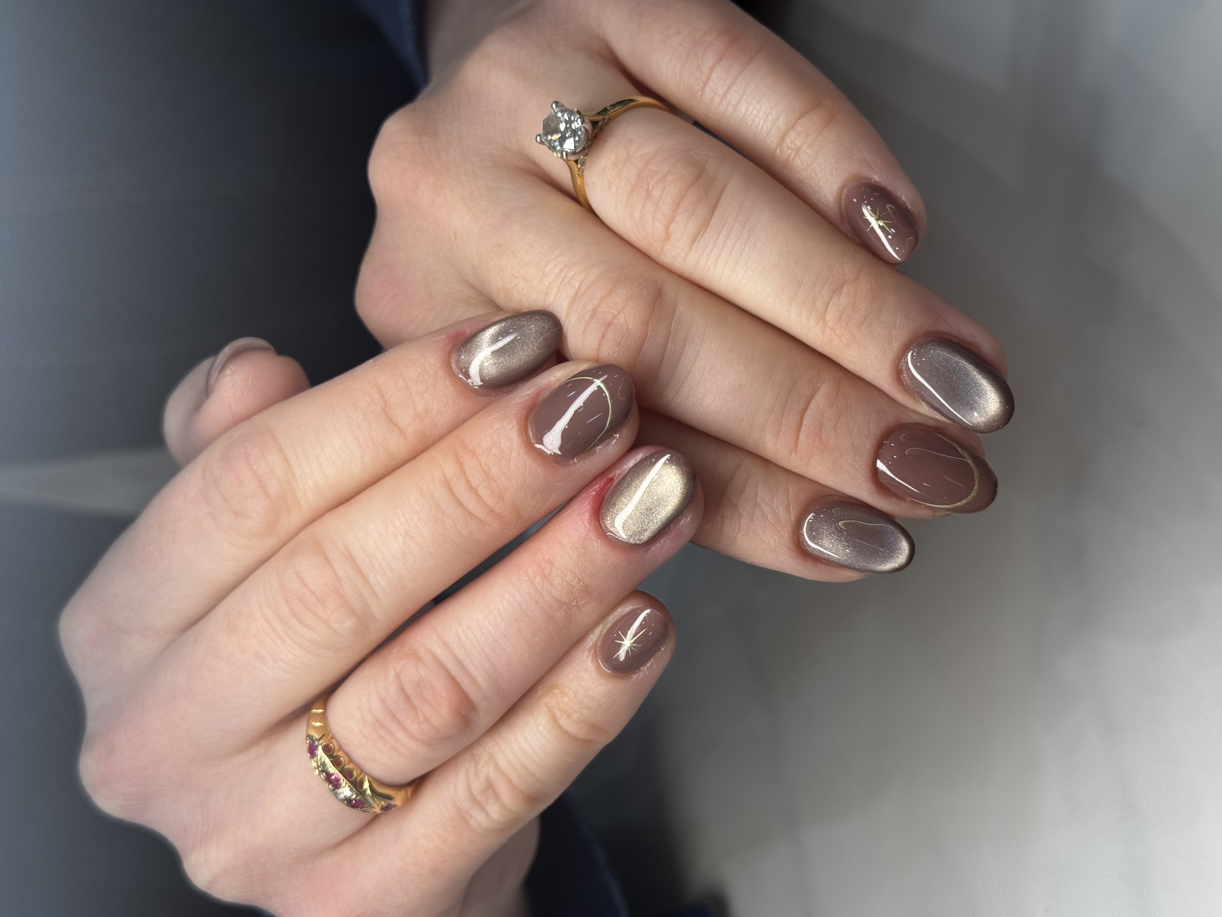 Short rounded nails in shimmering cat-eye brown with fine gold lines and stars