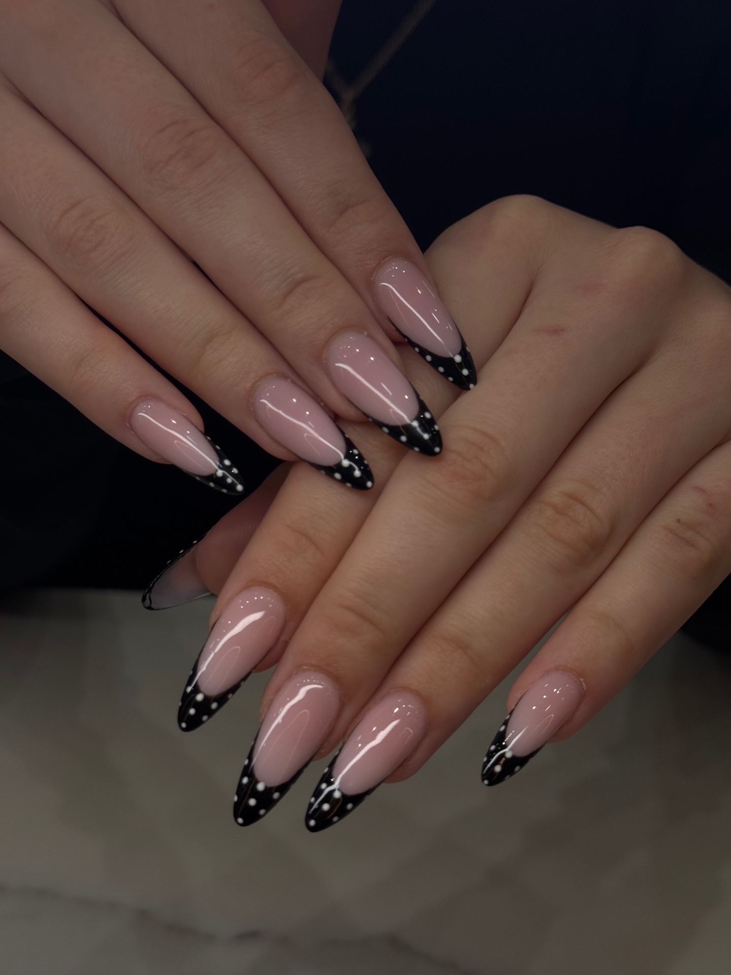 Almond nails with glossy black French tips and tiny white pin dots
